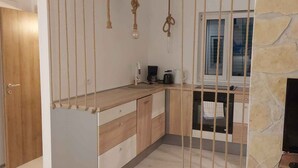Een kleine keuken met houten kastjes, een aanrecht, een raam en een stenen muur.