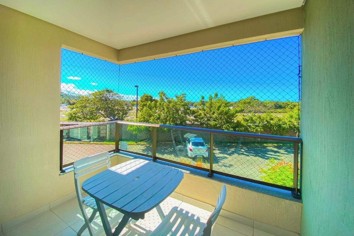 A balcony with a table and chairs, a car in the background, and a clear view of the surrounding area.
