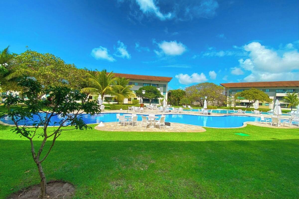 A resort with a large swimming pool surrounded by lounge chairs and palm trees.