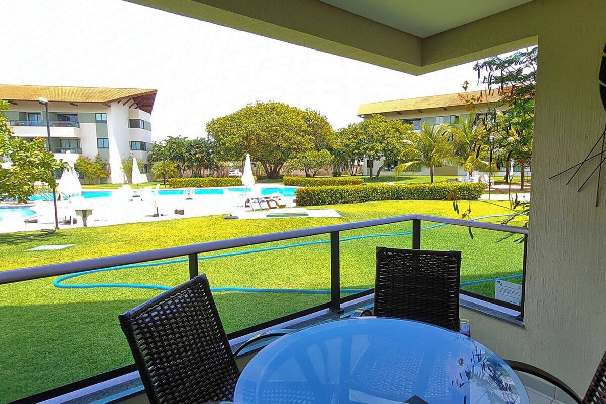 A balcony with a table and chairs, overlooking a swimming pool and a well-maintained lawn.