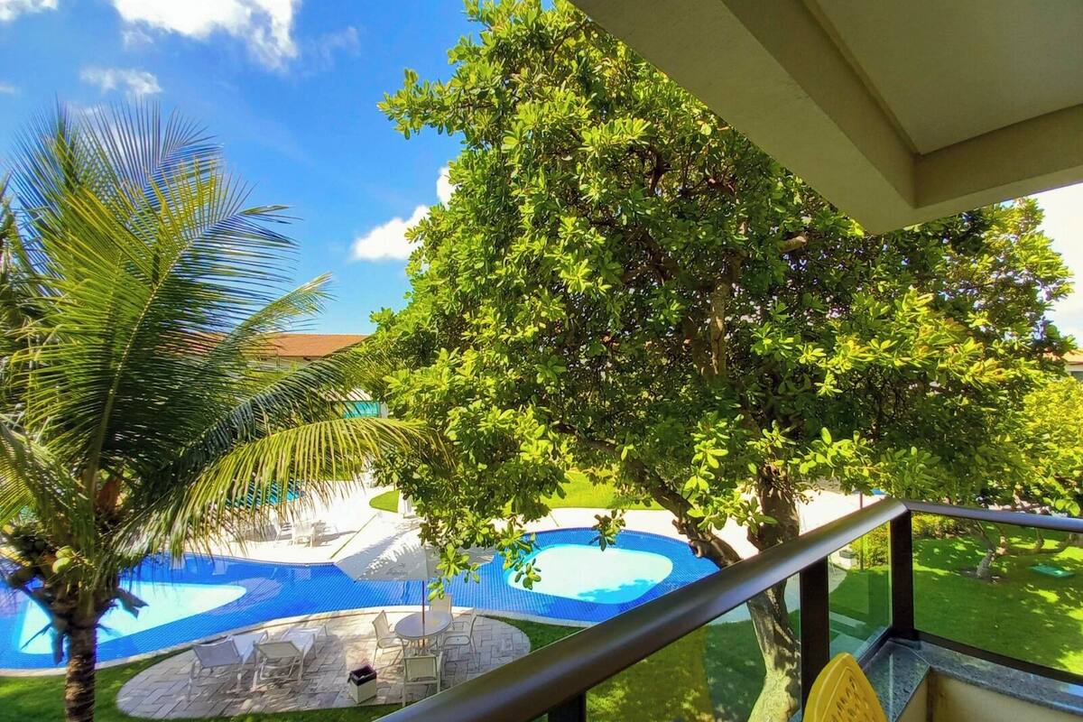 A pool area with a palm tree, a large tree, and a view of a building.