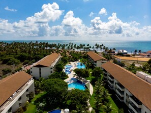 Ein Resort mit einem zentralen Schwimmbecken, mehreren Gebäuden mit roten Ziegeldächern und Blick auf den Ozean.