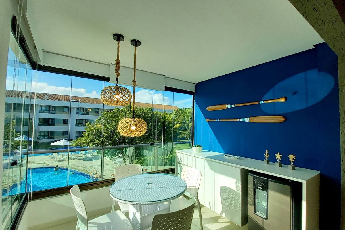 A modern room with a glass balustrade overlooking a pool, a round table with chairs, and a blue accent wall with wooden paddles.
