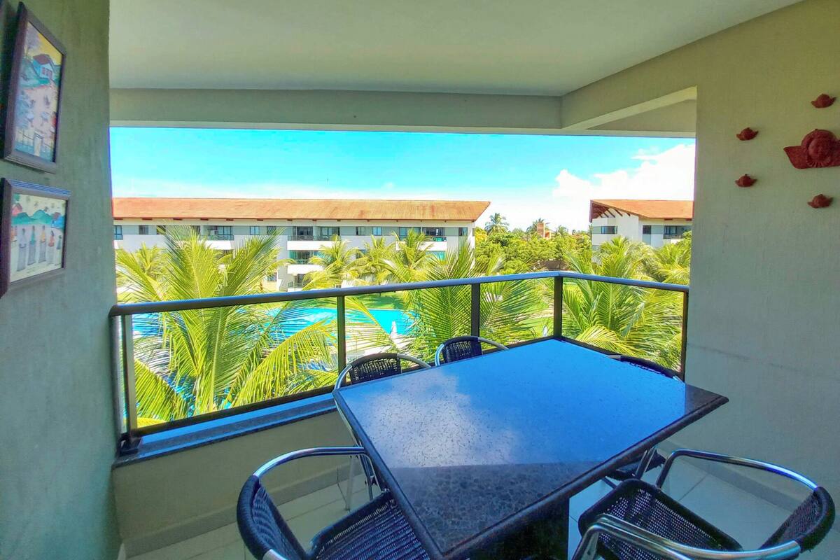 A balcony with a table and chairs, overlooking a pool and palm trees.
