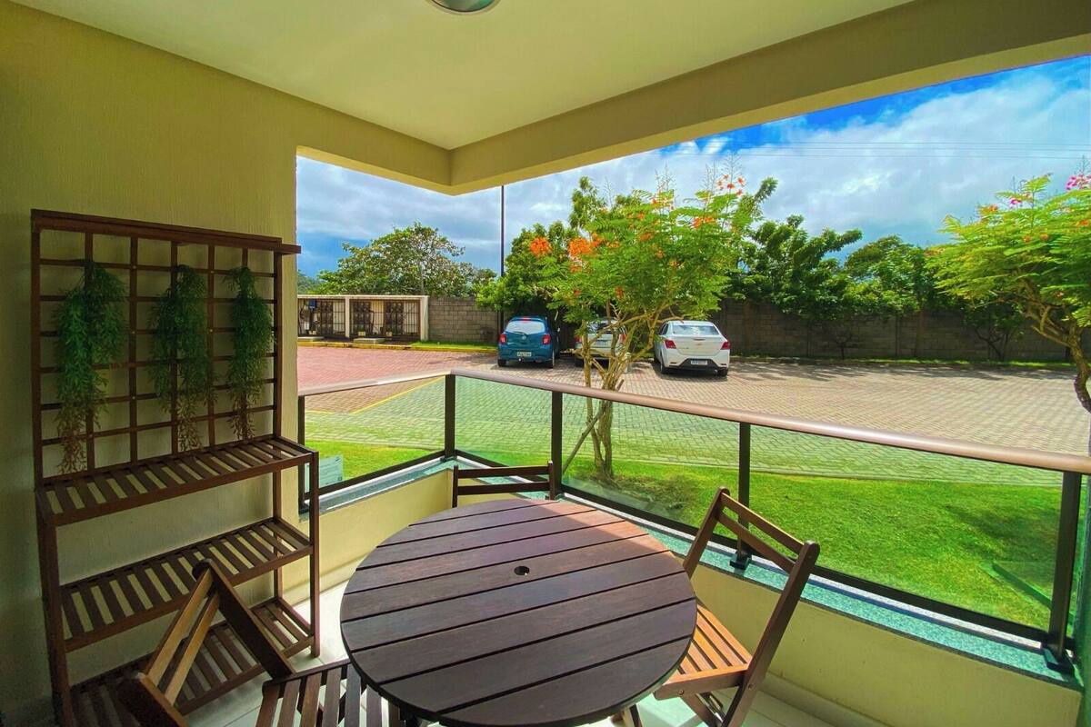 A balcony with a table and chairs, a view of a parking area, and a building with a green roof.