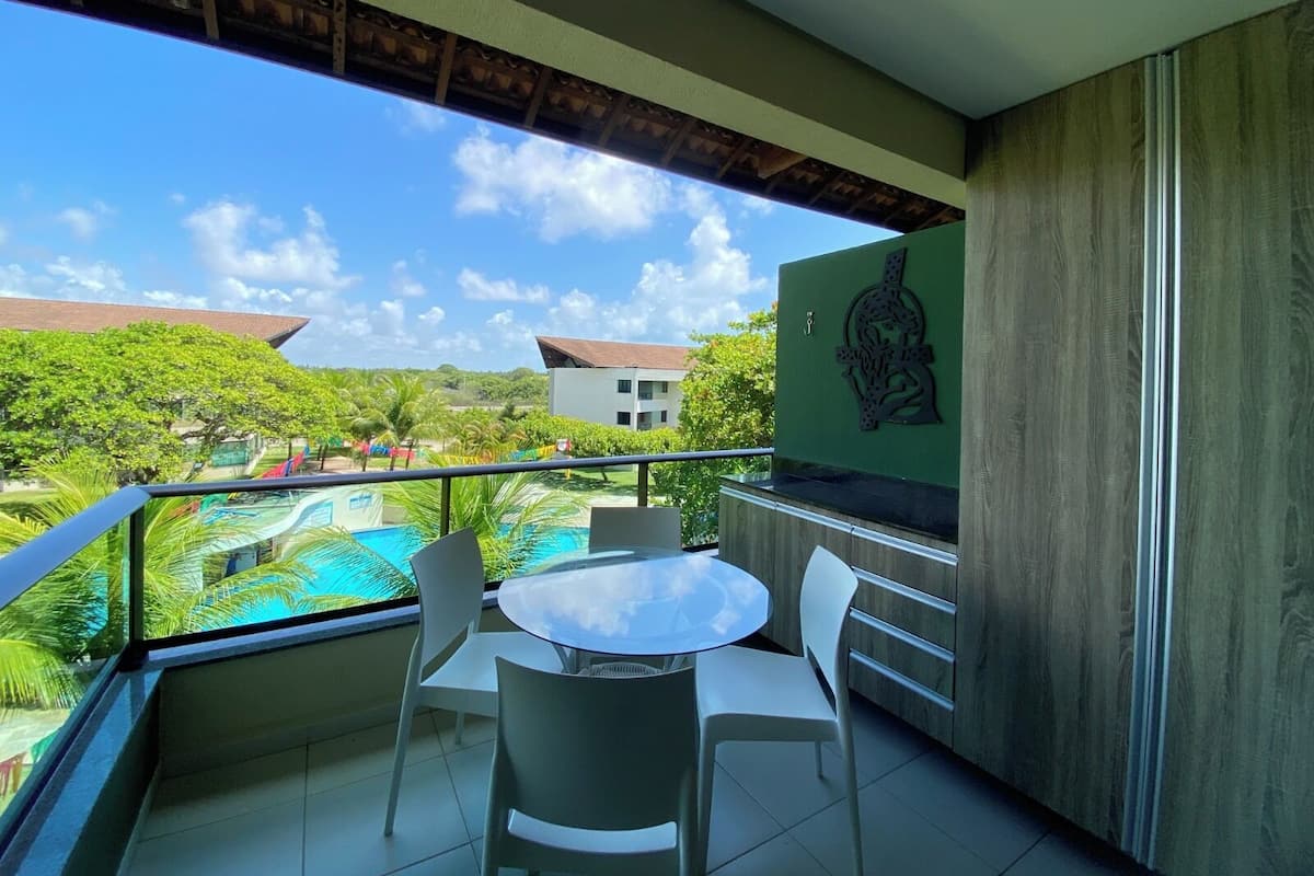 A balcony with a table and chairs, overlooking a swimming pool and lush greenery.