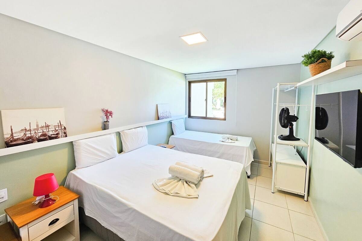 A hotel room with two beds, a small desk, a TV, and a window.