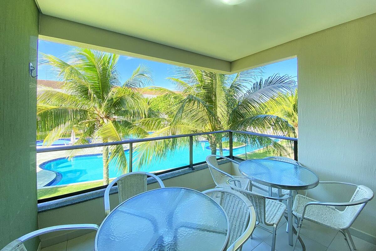 A balcony with a pool view, featuring white wicker furniture and a clear blue sky.