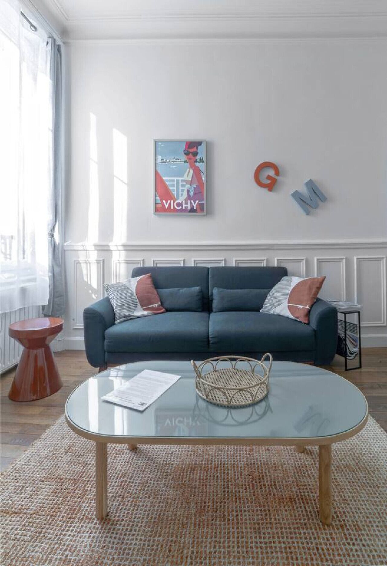 A living room with a dark blue sofa, a glass coffee table, and a poster on the wall.