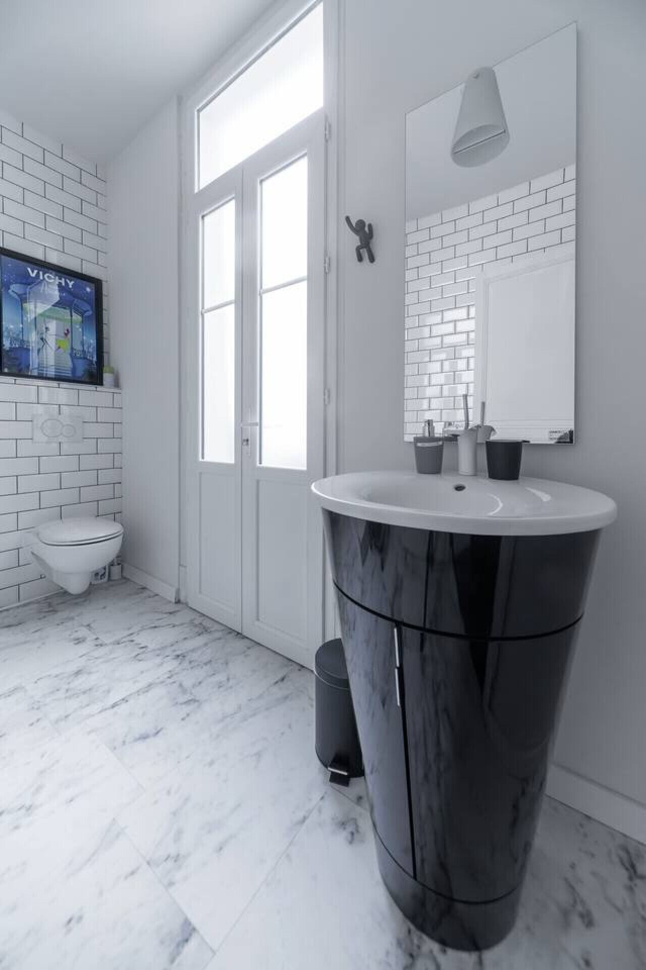 Een moderne badkamer met een witte backsplash van metro tegels, een marmeren vloer, een groot wastafelmeubel met een zwart wastafel en een toilet.
