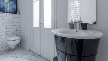 Een moderne badkamer met een witte backsplash van metro tegels, een marmeren vloer, een groot wastafelmeubel met een zwart wastafel en een toilet.
