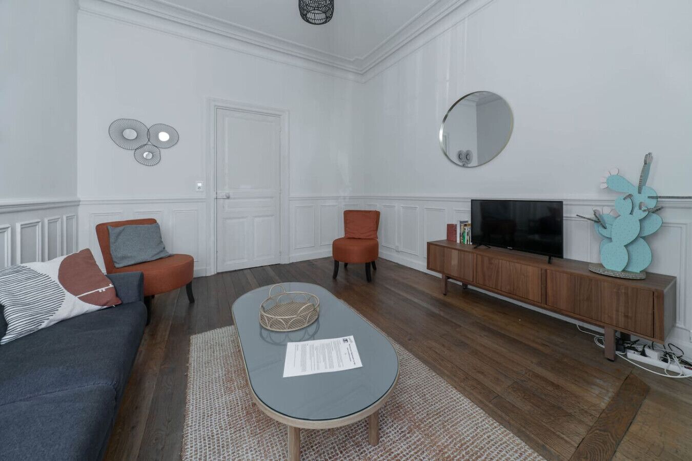 Een moderne woonkamer met een bank, twee fauteuils, een salontafel, een televisie en een houten kast.