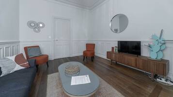 Een moderne woonkamer met een bank, twee fauteuils, een salontafel, een televisie en een houten kast.