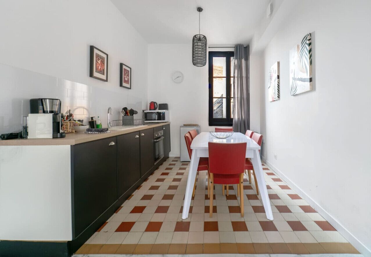 Een compacte keuken met een eethoek, met een zwart-wit geruite vloer, een eettafel met stoelen en een hanglamp.