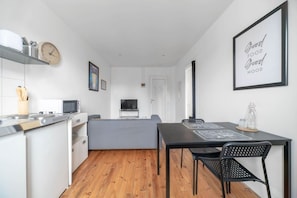 A modern kitchen with a dining area, wooden flooring, and a TV in the background. - Appartement lumineux en centre ville avec parking (Vichy)