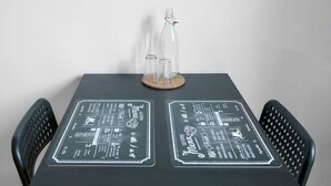 Une pancarte encadrée avec le texte « BONNE NOUVELLE, BONNE AMBIANCE » au-dessus d’une table sur laquelle sont posés des menus écrits à la craie.