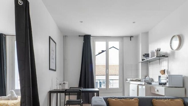 Un salon moderne et bien éclairé, avec un canapé gris, un plancher en bois et un coin repas comprenant une table et des chaises.