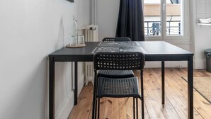 Une petite pièce moderne avec un plancher en bois, une table en métal noir, deux chaises noires, une citation encadrée accrochée au mur et une fenêtre donnant sur l’extérieur.