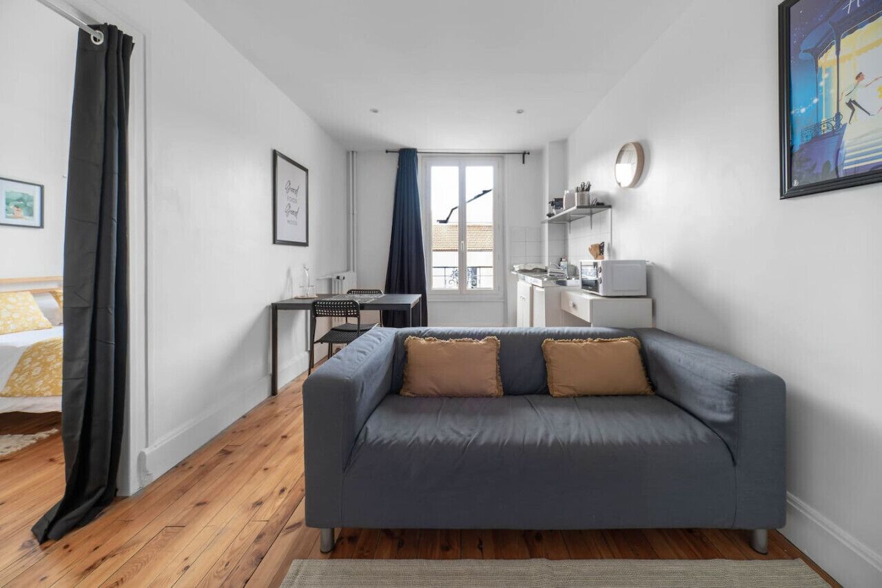 A compact living space with a grey sofa, a small dining table, and a kitchenette.