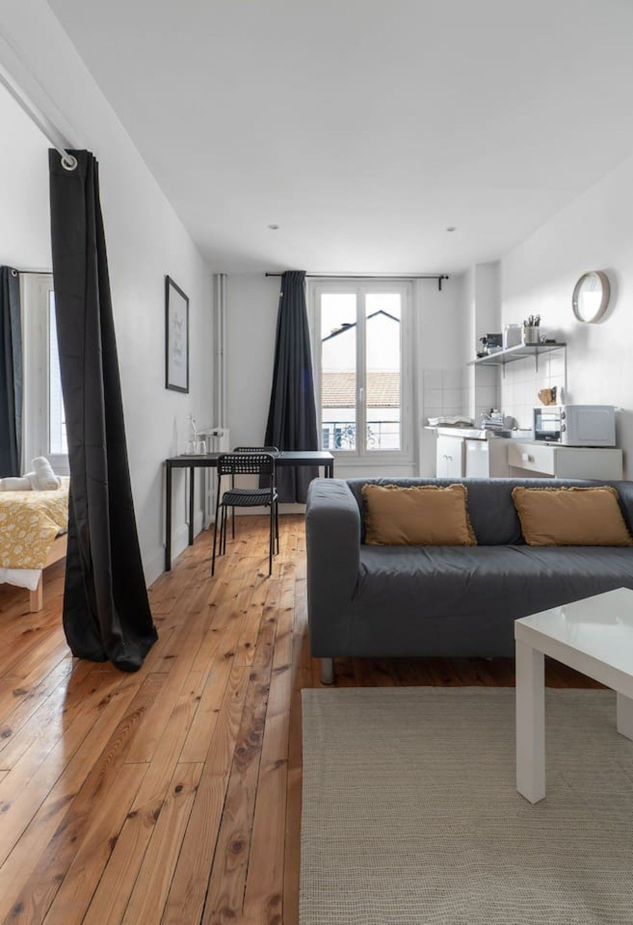 A modern living room with a grey sofa, wooden flooring, and a dining area with a table and chairs.