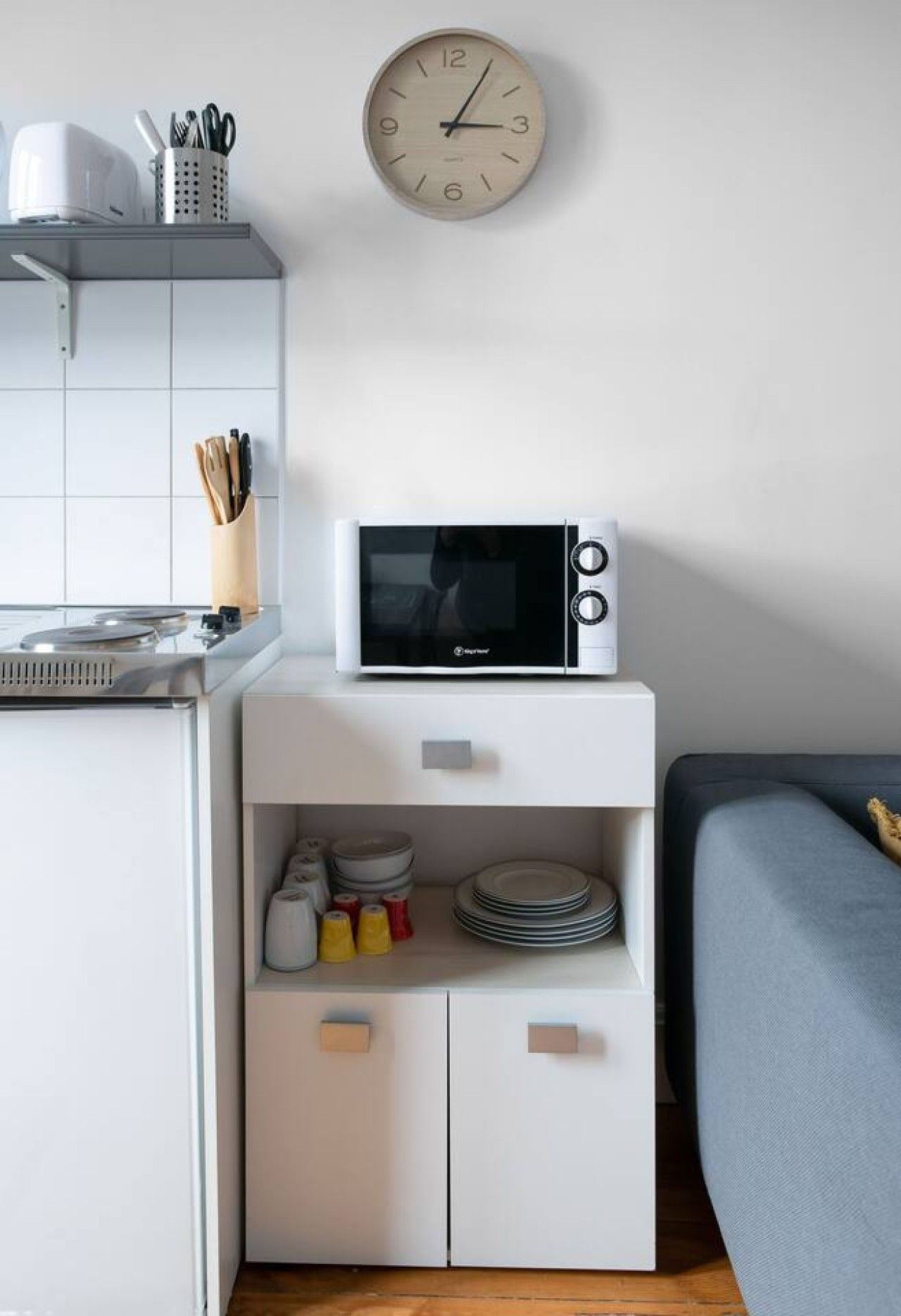 A compact kitchenette with a microwave, a clock, and storage cabinets.