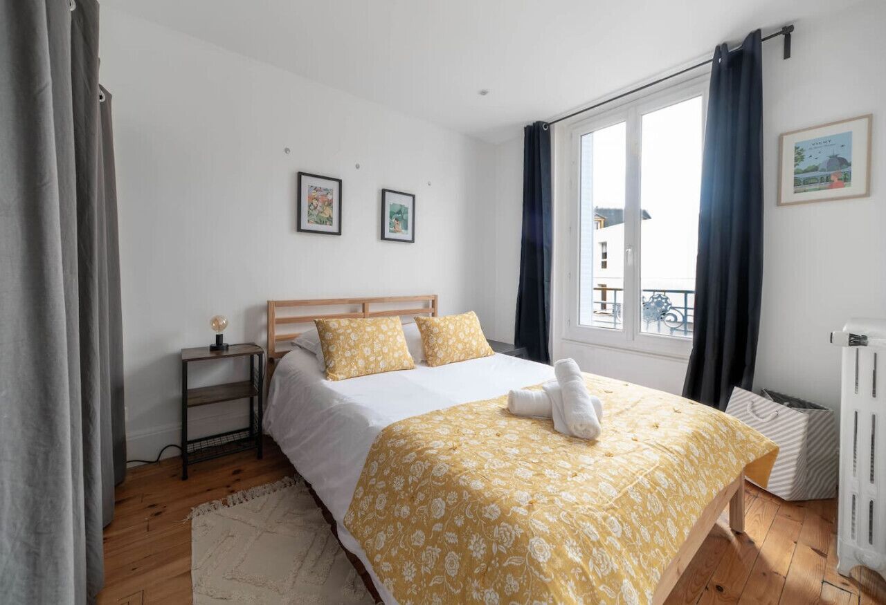 Een slaapkamer met een houten bed, een nachtkastje met een lamp en een raam met gordijnen.