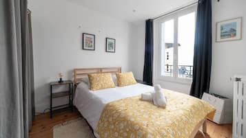 Een slaapkamer met een houten bed, een nachtkastje met een lamp en een raam met gordijnen.