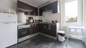 Une cuisine de taille réduite, équipée d’un réfrigérateur, d’une cuisinière, d’un four à micro-ondes et de meubles de rangement de couleur sombre.