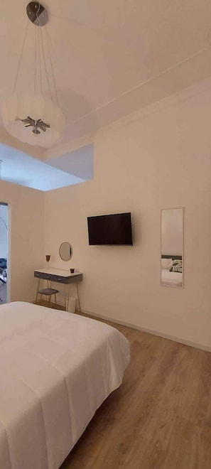 Quarto com cama, escrivaninha com espelho, TV de tela plana e uma pequena janela.