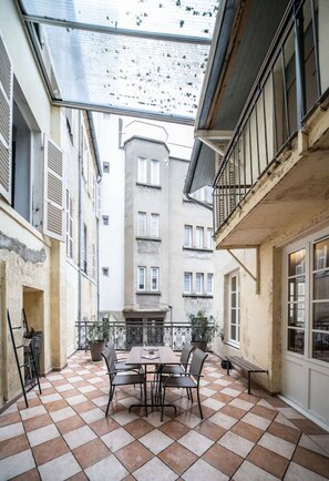 A courtyard with a checkered floor, a dining table with chairs, and a potted plant. - Superbe studio avec terrasse dans immeuble classé (Vichy)