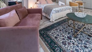 A modern bedroom with a large bed, a pink sofa, and a dining area with a table and chairs. - Superbe studio avec terrasse dans immeuble classé (Vichy)