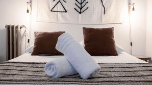 Una cama bien hecha con una toalla enrollada, dos almohadas marrones y un tapete a rayas.