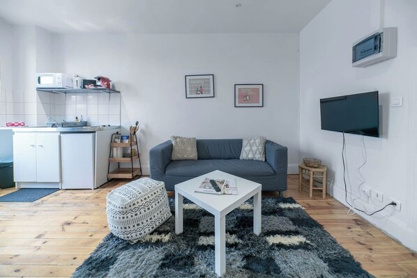 A modern living room with a grey sofa, a white coffee table, a patterned ottoman, and a flat-screen TV mounted on the wall.