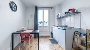 Une cuisine de taille réduite avec un coin repas, une horloge au mur et une vue par la fenêtre.