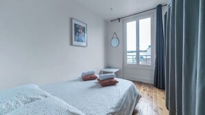Une chambre avec deux lits, une fenêtre avec des rideaux, une petite table et un miroir fixé au mur.