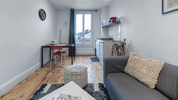 Un espace de vie compact comprenant un coin cuisine, un coin repas et un canapé agrémenté d’un coussin décoratif.