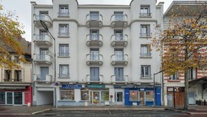 Un immeuble à plusieurs étages, doté d’une façade sobre, de nombreux balcons et de boutiques au rez-de-chaussée.