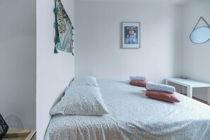 A bedroom with two beds, a small bedside table, a wall-mounted mirror, and a poster.