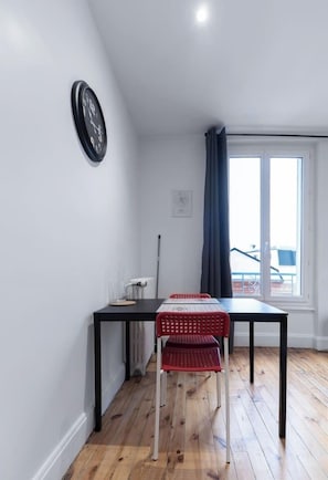 A room with a dining table, chairs, a clock, a radiator, and a window with curtains.
