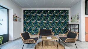 Una habitación con un ventanal grande, un tapiz tejido y una pared con un diseño de hojas tropicales.