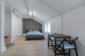 Un dormitorio con cama, mesa y silla. Hay una ventana y una puerta.