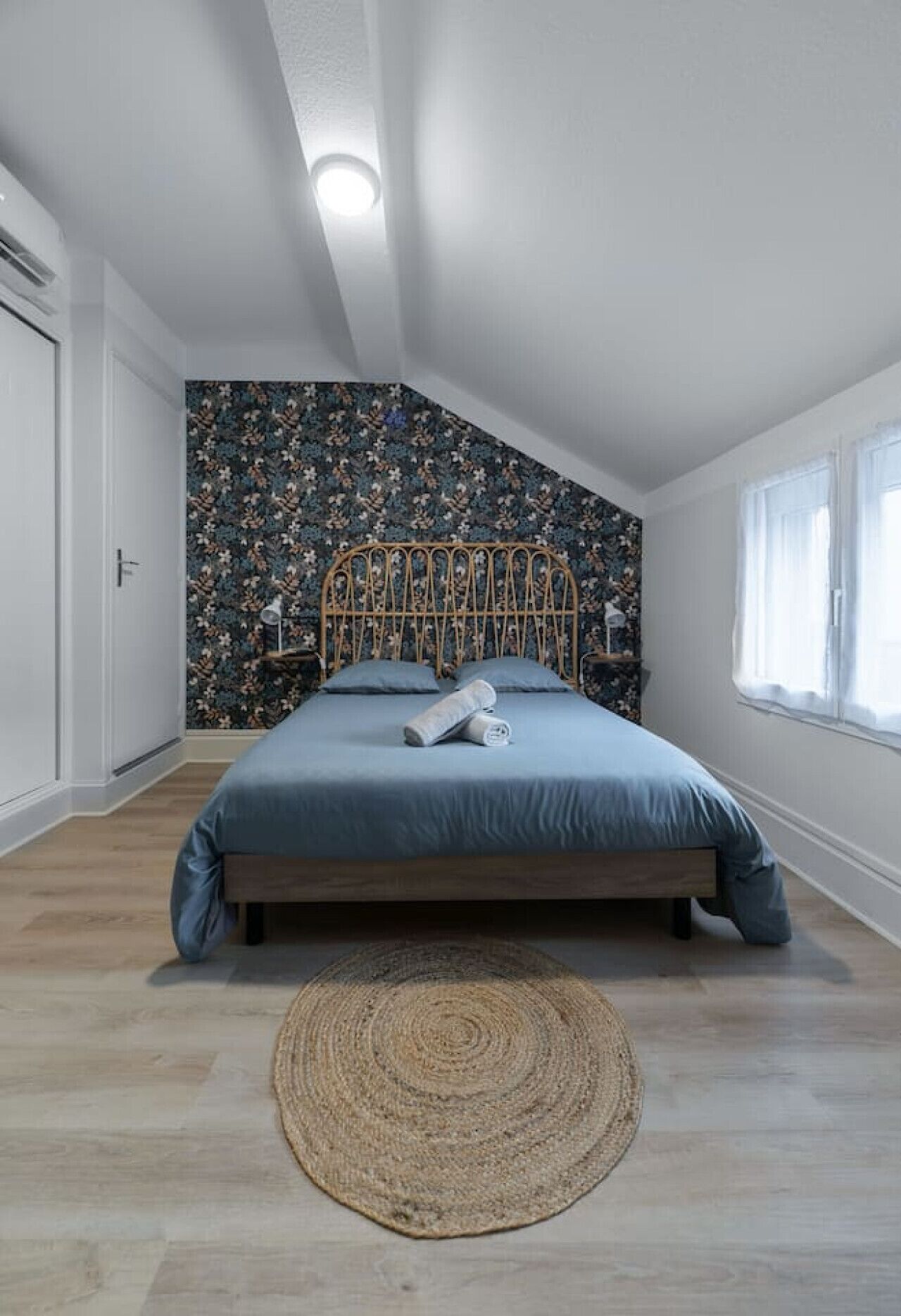A bedroom with a bed, a woven rug, and a floral-patterned wall.