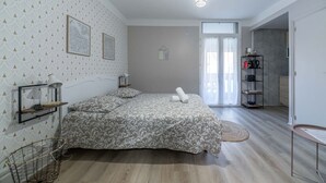 A bedroom with a bed, a bedside table, a lamp, a map on the wall, and a door leading to another room.