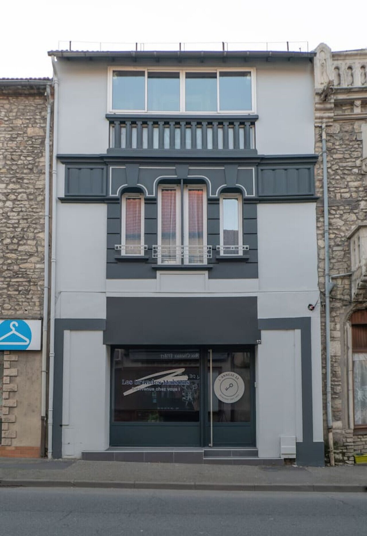 Ein zweistöckiges Gebäude mit moderner Fassade, mit einem großen Schaufenster und einem hängenden Schild, das auf ein Bekleidungsgeschäft hinweist.