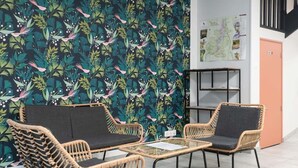 A room with a patterned wall, two wicker chairs with black cushions, a small round table, and a woven rug.