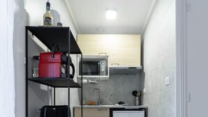 A narrow hallway with a kitchenette area featuring a microwave, a small refrigerator, and a shelf with various items.