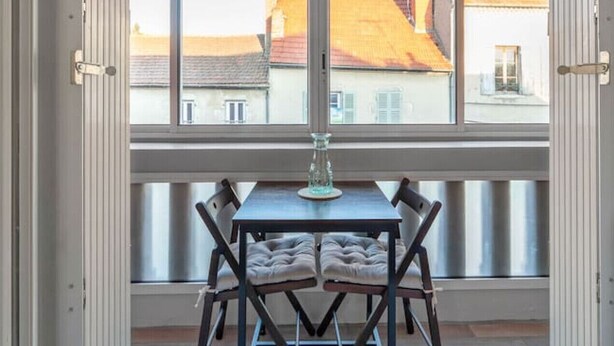 A dining area with a table and chairs, large windows with a view of buildings, and a hanging light fixture.