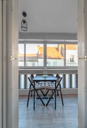 Un comedor con una mesa y sillas, ventanas amplias con vista a edificios, y una lámpara colgante.