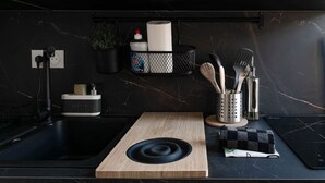A modern kitchen with a black countertop, a wooden cutting board, a sink, and a black induction cooktop.