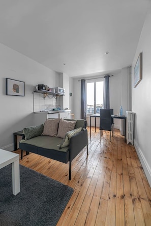 A modern living room with a sofa, a dining table, and a kitchen area with a microwave. - Appartement design en centre ville (Vichy)